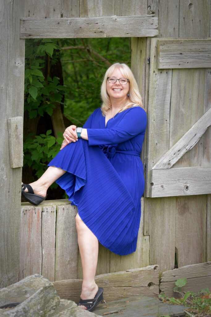 A woman in blue dress sitting on the side of a barn.