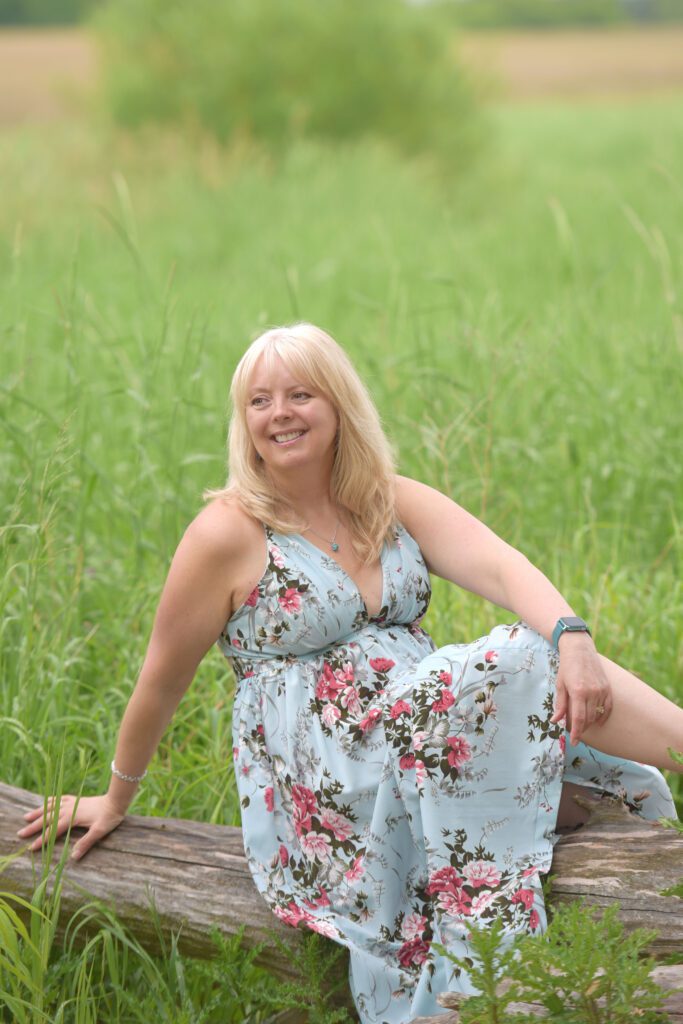 A woman sitting on top of a log in the grass.